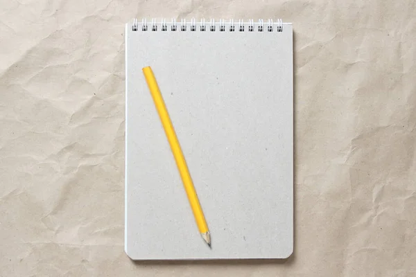Szary notatnik z białą zwiniętą sprężyną i ołówkiem na tle beżowego pogniecionego papieru rzemieślniczego — Zdjęcie stockowe