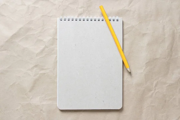 Gray notepad with white coiled spring and pencil on a background of beige crumpled craft paper