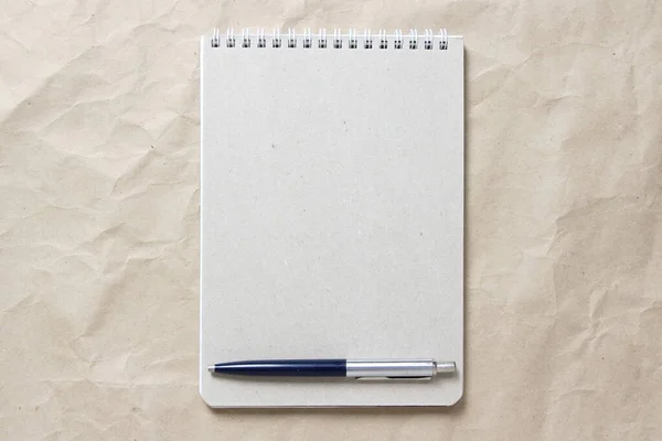 Bloc-notes gris avec ressort enroulé blanc et stylo sur fond de papier artisanal froissé beige — Photo