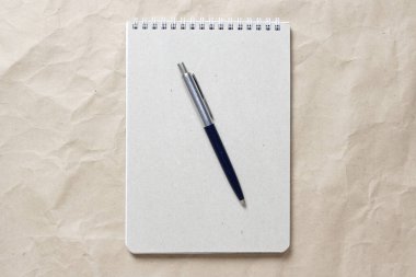  Beyaz sarmalanmış yay ve arkaplandaki bej buruşuk el işi kağıdının üzerindeki kalemle gri not defteri.