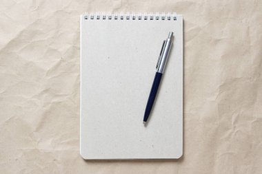  Beyaz sarmalanmış yay ve arkaplandaki bej buruşuk el işi kağıdının üzerindeki kalemle gri not defteri.