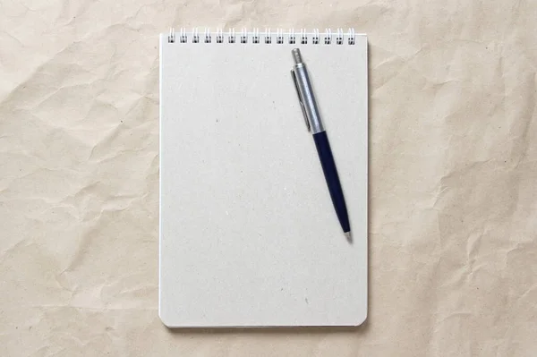 Blocco note grigio con molla a spirale bianca e penna su uno sfondo di carta artigianale spiegazzata beige — Foto Stock