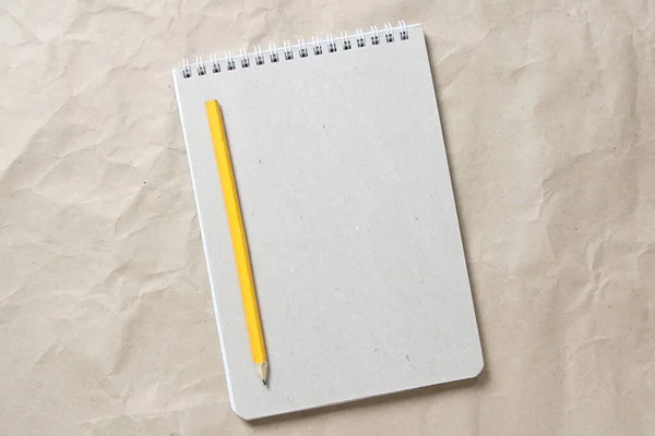 Gray notepad with white coiled spring and pencil on a background of beige crumpled craft paper