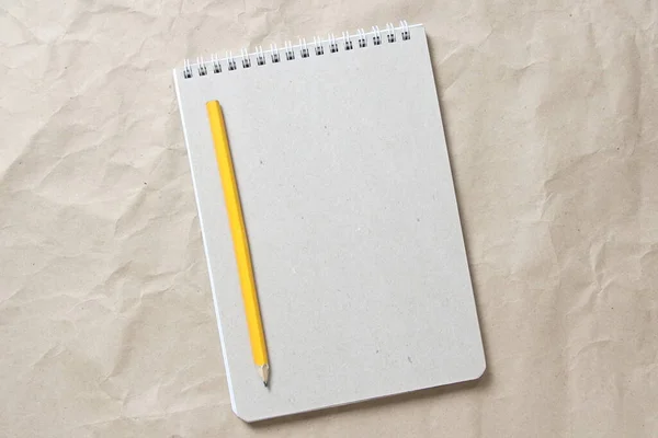 Szary notatnik z białą zwiniętą sprężyną i ołówkiem na tle beżowego pogniecionego papieru rzemieślniczego Obraz Stockowy