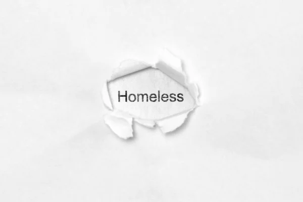 Slovo bezdomovec na bílém izolovaném pozadí skrz díru po ráně v papíru. — Stock fotografie