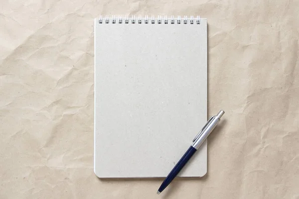 Gray notepad with white coiled spring and pen on a background of beige crumpled craft paper