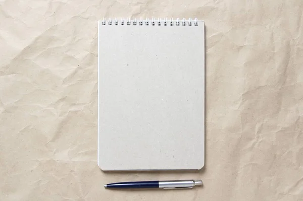 Bloc-notes gris avec ressort enroulé blanc et stylo sur fond de papier artisanal froissé beige — Photo