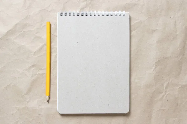 Gray notepad with white coiled spring and pencil on a background of beige crumpled craft paper — Stock Photo, Image