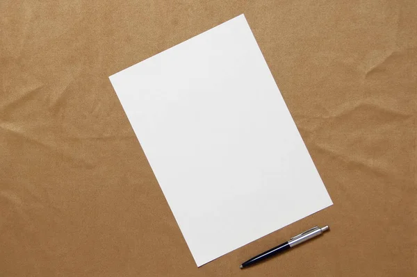 Modèle de papier blanc avec stylo se trouve en diagonale sur fond de tissu brun clair. Concept de plan d'affaires et de stratégie. Photo de stock avec espace vide pour le texte et le design — Photo