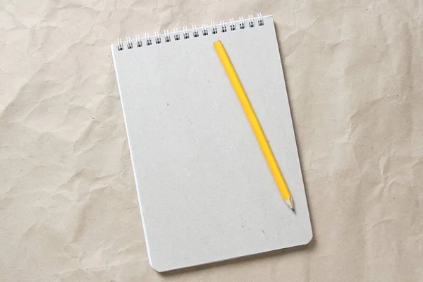 Γκρι σημειωματάριο με λευκό τυλιγμένο ελατήριο και μολύβι σε φόντο από μπεζ τσαλακωμένο χαρτί χειροτεχνίας — Φωτογραφία Αρχείου