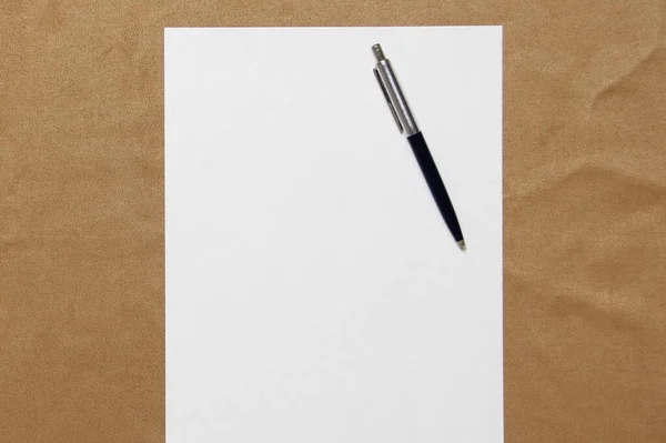 Modelo de papel branco com caneta encontra-se no fundo de pano marrom claro. Conceito de plano de negócios e estratégia. Foto stock com espaço vazio para texto e design — Fotografia de Stock