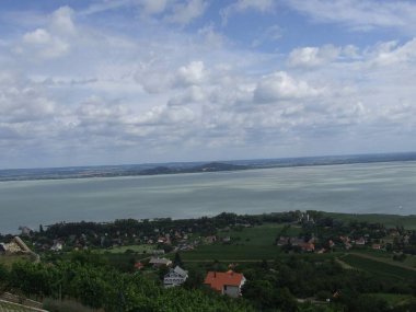 Sakin göl, yeşil üzüm bağları ve manzarayı noktalayan antika evlerle çevrili gökyüzünü yansıtıyor. Huzurlu bir kırsal alan oluşturuyor..