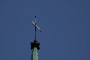Kilisenin yükselen kulesi gururla parlak mavi gökyüzüne karşı duruyor. Dekoratif rüzgar gülü, öğle rüzgarında hafifçe dönüyor. Karmaşık tasarım detaylarını gözler önüne seriyor..