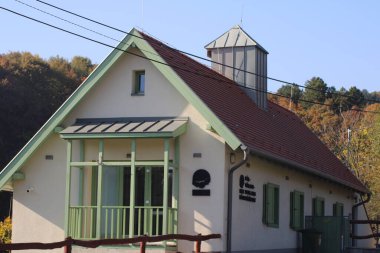 Huzurlu bir kırsal alanda, canlı yeşillikler ve dingin tepelerle çevrili, sıcak güneş ışığıyla yıkanmış, farklı bir kuleye sahip tuhaf bir ev duruyor..