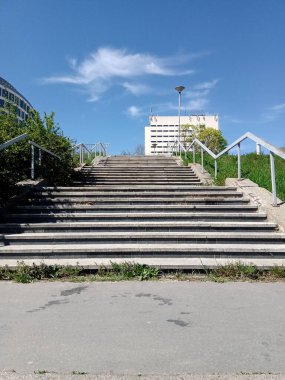 Çağdaş mimarinin yanındaki canlı yeşil alana doğru yükselen bir dizi beton merdiven berrak mavi gökyüzüne karşı parlak güneş ışığıyla yıkanır..
