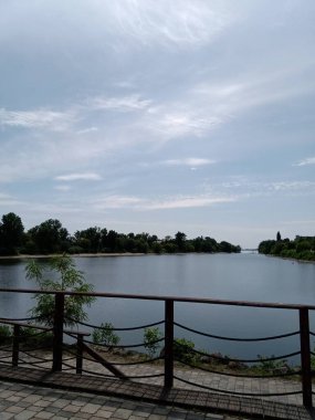 Sakin bir nehir kenarı manzarası, açık bir su yolu içerir. Mavi gökyüzünün altında, hafif bulutlarla çevrili. Rahatlamak için huzurlu bir atmosfer yaratır..