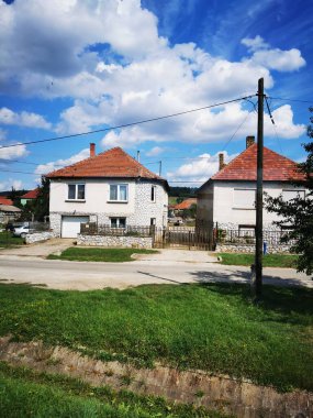 Kırmızı çatıları olan iki beyaz ev huzurlu bir kırsal alanda yan yana oturuyorlar. Sahnede bulutları kabarık, berrak, mavi bir gökyüzü var, sakin bir atmosfer yaratıyor..