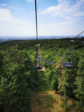 Bir teleferik canlı yeşil bir ormanın içinden yükselir, berrak gökyüzü ile aydınlık bir günde çevrenin büyüleyici manzarasını gözler önüne serer..