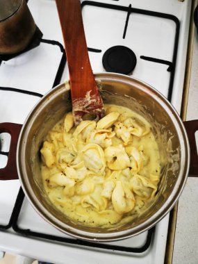 Kremalı sosta pişen tortellini dolu bir tencere sobanın üstünde duruyor. Tahta bir kaşık makarnayı karıştırıyor, rahatlatıcı bir yemek hazırlıyor..