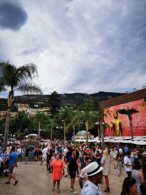 Canlı bir kalabalık, palmiye ağaçları ve bulutlu bir yaz gökyüzü altında çarpıcı dağ manzaralarıyla çevrili, kıyı kasabasında hareketli bir atmosferin keyfini çıkararak, canlı bir açık hava deneyimi yaratıyor..