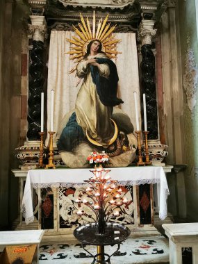 Sunakta, bir kilisenin zengin dekore edilmiş zeminine karşı mumlar ve zarif çiçeklerle çevrili, çarpıcı bir Bakire Meryem heykeli sergileniyor..