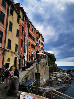 Ziyaretçiler, okyanusa bakan canlı binaların yanında yürür, parçalı bulutlu bir öğleden sonra büyüleyici sahil manzarasının tadını çıkarırlar..