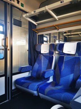 Bir tren vagonunun içinde mavi desenli koltuklar bulunur, güneş ışığı boş alanı aydınlatır ve çağdaş tasarımı ön plana çıkarır..