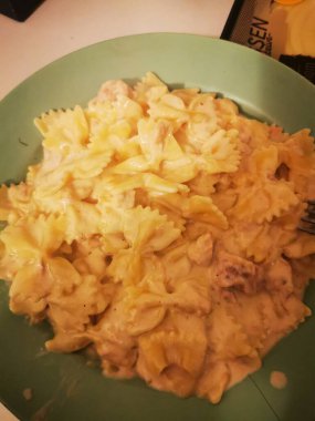 Sıcak bir tabak kremalı makarna. İçinde tavuk parçaları ve zengin bir sos var. Mutfak tezgahındaki yeşil bir kasede oturmuş, eğlenmeye hazır..