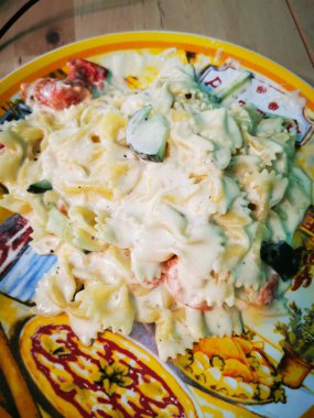 Papyonlu makarna ve taze sebzelerin yer aldığı kremalı makarna tabağı sıcak bir yemek ortamında canlı, dekore edilmiş bir tabakta sunuluyor..