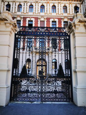 Karmaşık bir şekilde tasarlanmış demir kapı ziyaretçileri güzel detaylı tarihi bir binaya davet ediyor. Mimaride canlı renkler ve zarif motifler var, davetkar bir atmosfer yaratıyor..