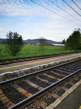 Sahnede, arka planda yumuşak tepeler ve yukarıda bulutlu bir gökyüzü bulunan ve barışçıl bir atmosferi taşıyan çimenli bir arazinin yanındaki demiryolu rayları yer alıyor..
