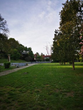Bu sakin parkta, yumuşak otlar, rüzgarda sallanan ağaçlar gibi zemini kaplar. Arka planda sönen akşamın ışıklarıyla aydınlanan tuhaf bir bina duruyor..