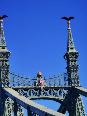 Budapeşte 'deki Özgürlük Köprüsü süslü tasarımı ve kartal heykelleriyle dimdik ayakta duruyor. Canlı mavi gökyüzü köprünün çarpıcı özelliklerini artırıyor, mimari zarafetini yansıtıyor..