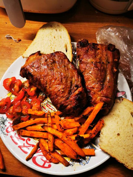 Juicy grilled meat is paired with crispy sweet potato fries and fresh sliced tomatoes, all presented on a colorful plate in a cozy dining setting.