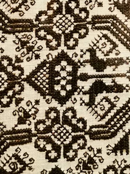 Текстиль демонстрирует сложные узоры, тщательно сотканные в черные нити на светлом фоне, отражающие богатое культурное наследие и мастерство.