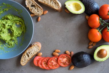 Kahverengi mermerden bir zemin üzerinde yeşilliklerle süslenmiş badem ve tostlarla süslenmiş Avokado Meyveleri macunu. Latin Amerika guacamole sosu sağlıklı yemek vejetaryen yeşil salatası