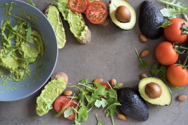 Kahverengi mermerden bir zemin üzerinde yeşilliklerle süslenmiş badem ve tostlarla süslenmiş Avokado Meyveleri macunu. Latin Amerika guacamole sosu sağlıklı yemek vejetaryen yeşil salatası