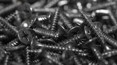 İnşaatın unsurları ve detayları. Bir sürü siyah vida. Yukarıdan bak. Doku. Geçmişi. İnşaat malzemeleri satışı. Bir grup kendini beceren vida etrafa saçılmış. Seçici odak