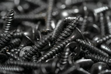 İnşaatın unsurları ve detayları. Bir sürü siyah vida. Yukarıdan bak. Doku. Geçmişi. İnşaat malzemeleri satışı. Bir grup kendini beceren vida etrafa saçılmış. Seçici odak