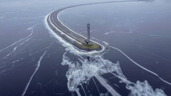 A lighthouse on a long dam frozen in ice cracks. Aerial view