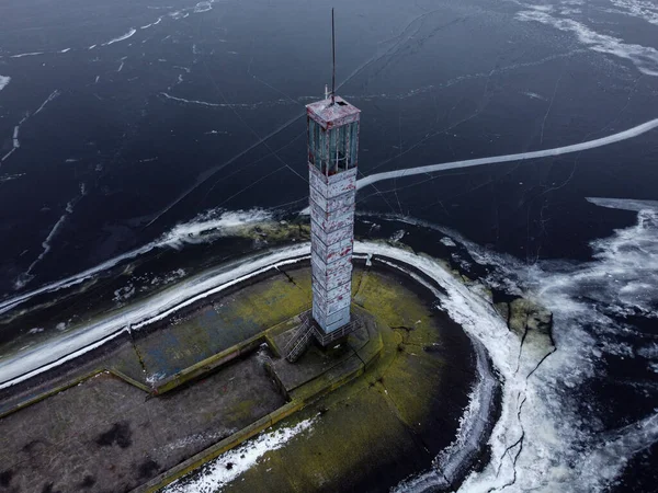 A lighthouse on a long dam frozen in ice cracks. Aerial view