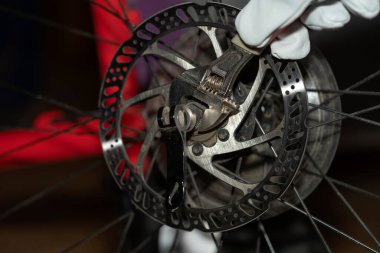 Bisikletin arka tekerleğini değiştirmek. Motorun teknik incelemesi. Kırmızı iş eldivenli bir ingiliz anahtarıyla bir bisiklet aracını sökmek