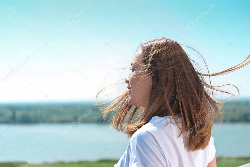 beautiful woman with messy hair blown by wind looking at landscape. riverside country tranquil place. staycations and weekend travelling. sunny weather. happy cheerful woman.