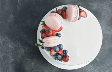 Üzerinde pembe badem kurabiyeleri, taze çilekler ve gri arkaplanda yaban mersinli güzel bir kremalı pasta. Kopyala. Tatil yemekleri. Doğum günü pastası..