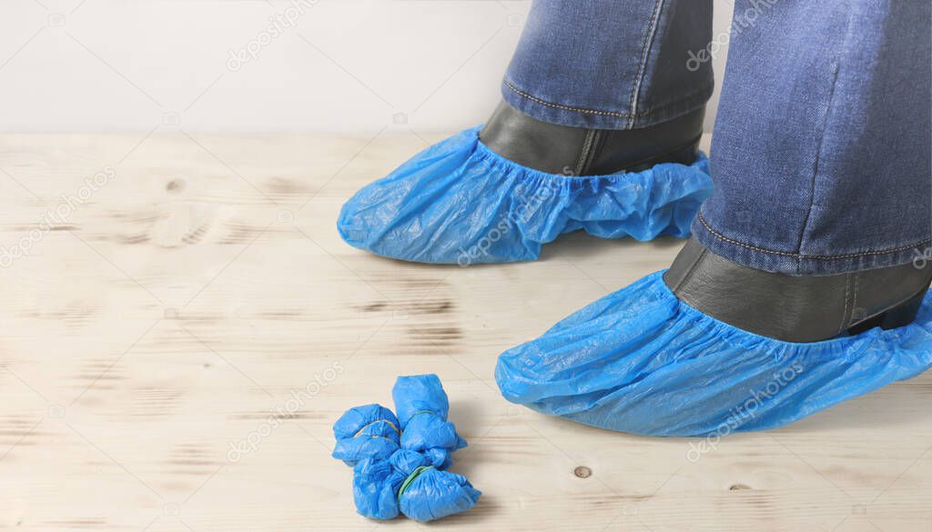 disposable blue shoe covers for hospital visits on woman's boots on wooden floor. woman wearing shoe covers for protection and cleanliness in medical office.