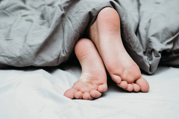 girl's feet covered with bed sheet. crop view of a girl in the bed sleeping tight. melatonin, circadian rhythms concept. healthy sleep of children.