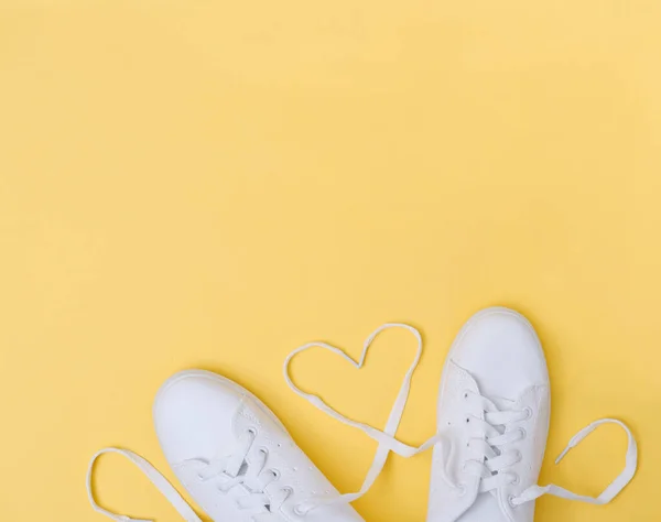 white sneackers with heart shaped laces on yellow background. love concept. blogging content. female teenager sporty casual footwear.