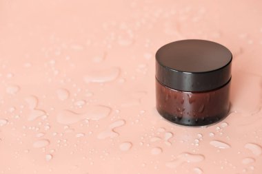 Bej arka planda cam kavanozda nemlendirici krem. Su bir kavanoza ve masaya damlıyor. Sıvı alma ve yüz bakımını tazeleme