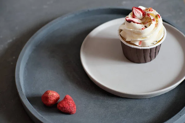 One cupcake decorated with cream frosting and dry sublimated strawberry. minimal style, concrete plates and grey background — 图库照片