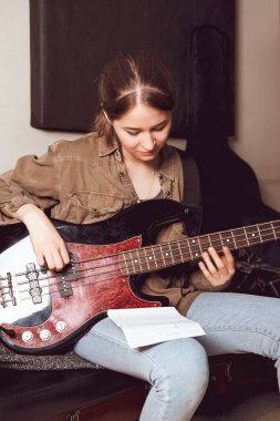 Genç bir kadın bas gitar çalıyor ve notalara bakıyor. Prova odası. Kadın rock müzisyeni. dikey boyut. 